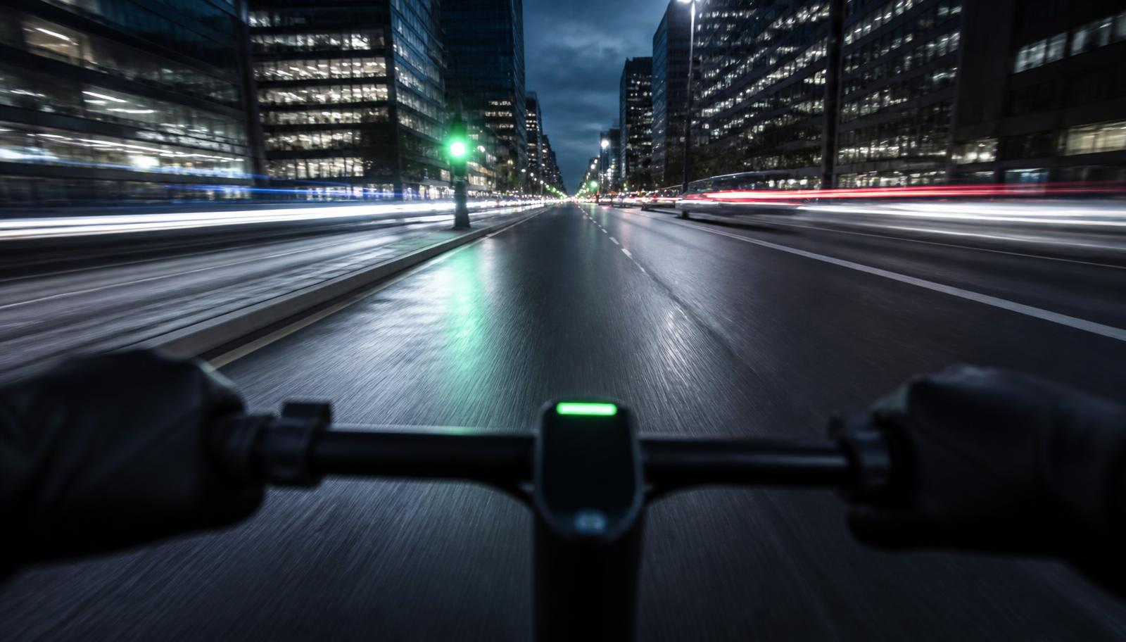 Vista desde el manillar de un patinete eléctrico circulando por una avenida iluminada